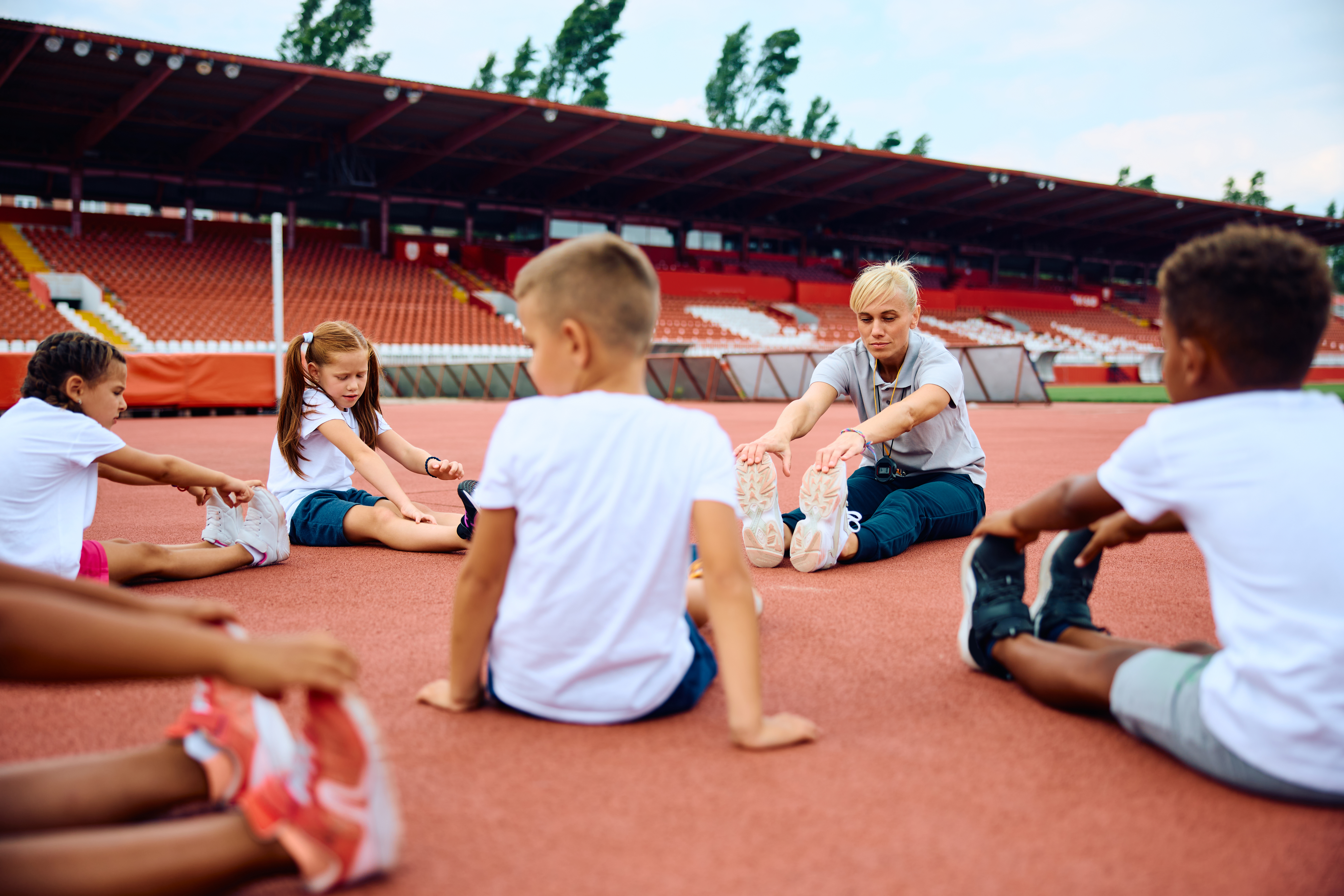 Children sitting down in a circle with their coach on a running track