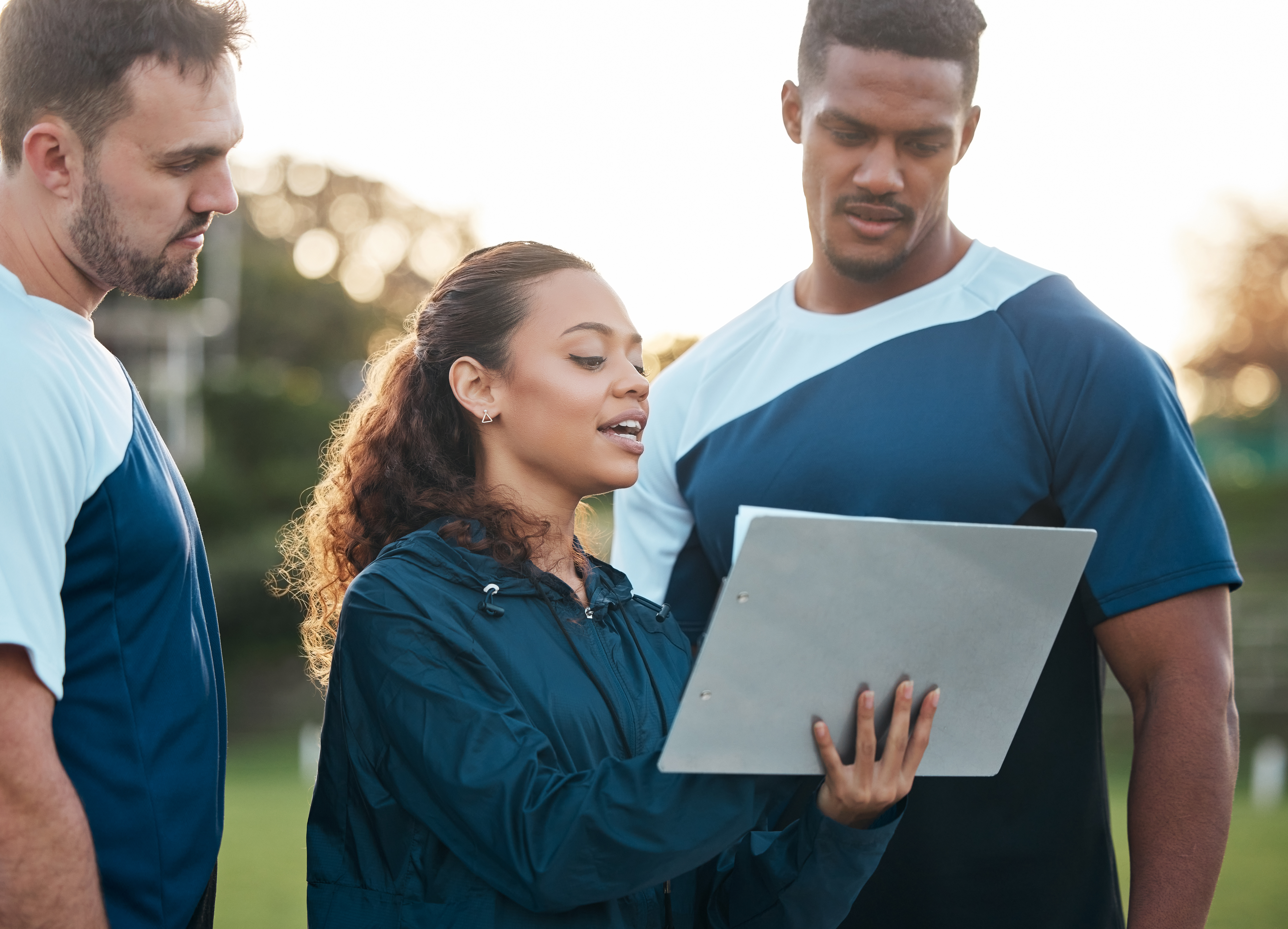 Woman looking at coaching board and speaking to 2 male athletes