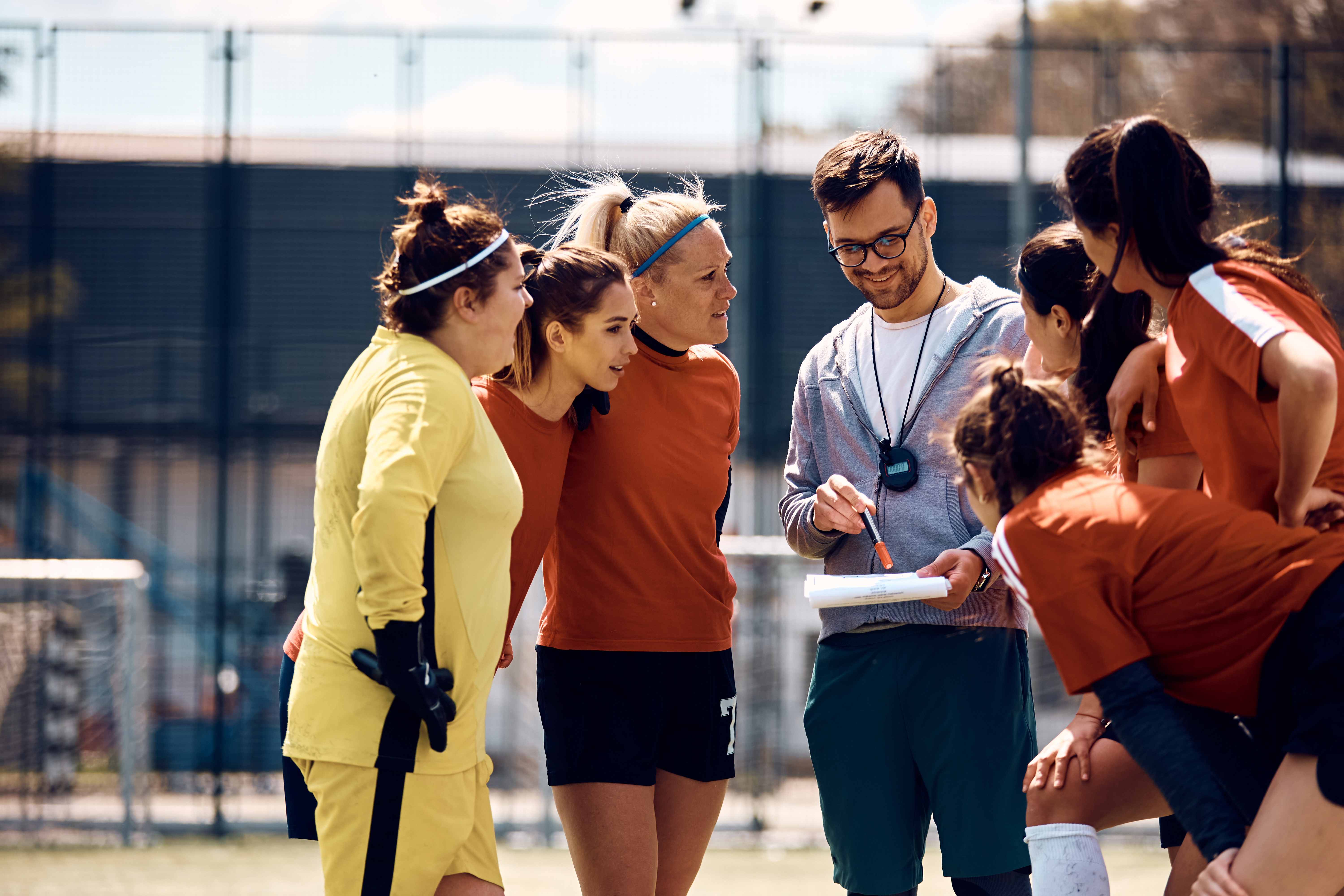 A man coaching several women at the side of a hockey pitch