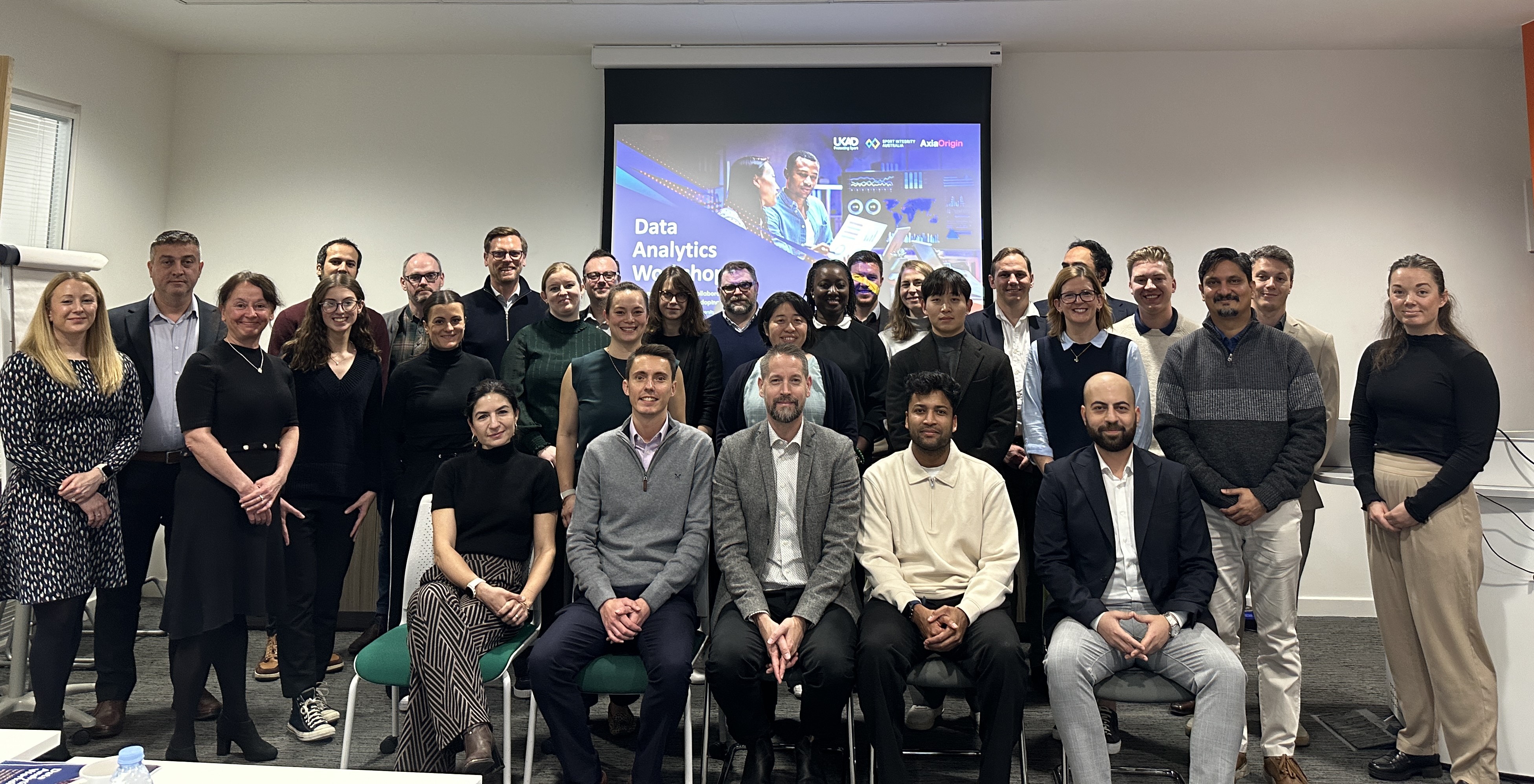 Delegates of the Analytics Workshop standing in front of a UKAD branded backdrop looking at the camera smiling